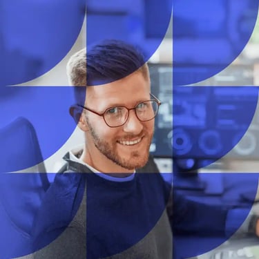 Smiling man with glasses wearing a dark sweater in an office setting with purple geometric overlay.